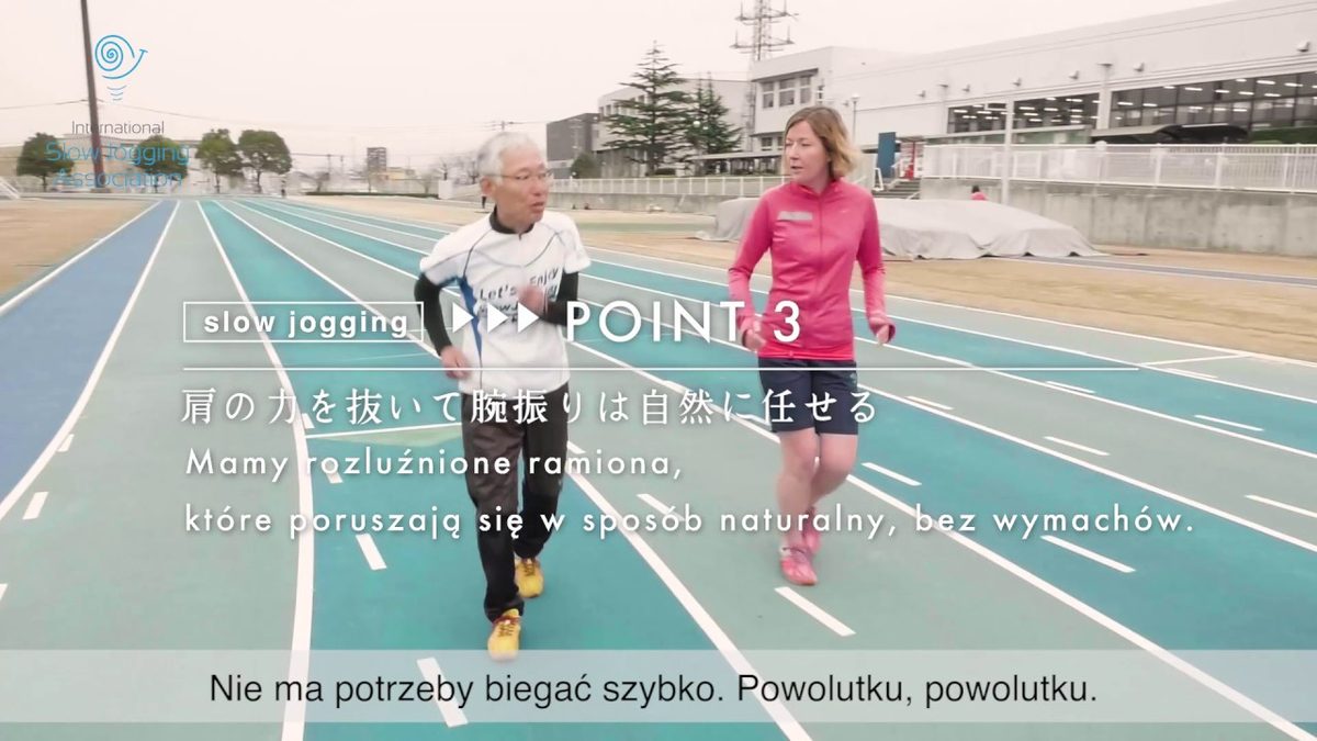 Hiroaki Tanaka in yellow shoes jogging on a running track beside a woman in pink, with Japanese and Polish captions on screen.
