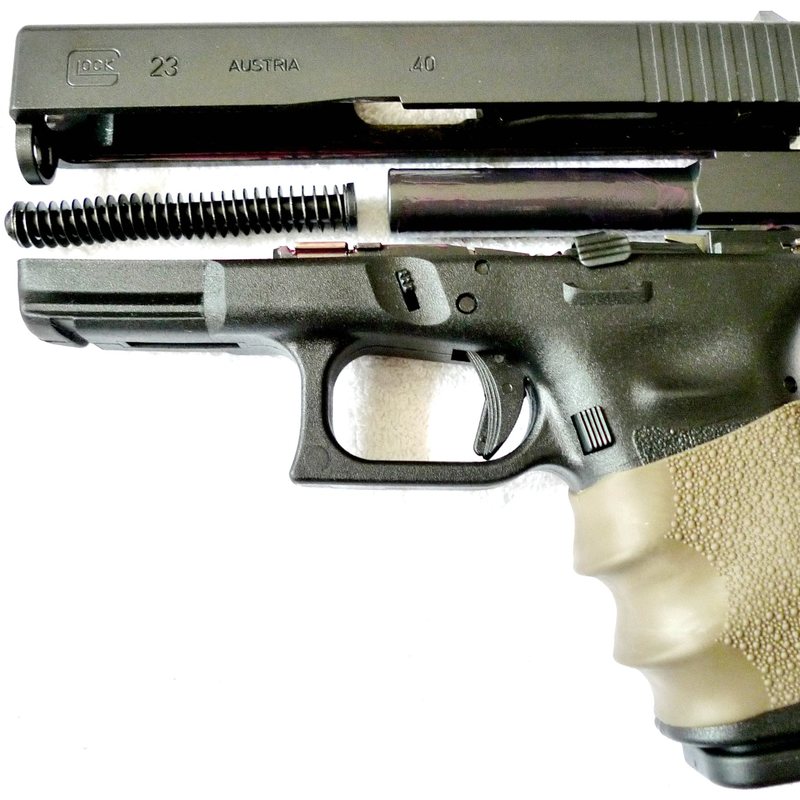 Close-up of a Glock 23 pistol with its slide partly off, showing the spring, and a rubber grip sleeve.