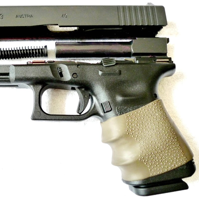 Close-up of a Glock 23 pistol with its slide partly off, showing the spring, and a rubber grip sleeve.