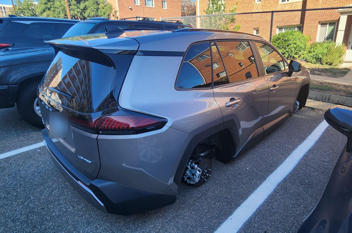 A new gray Toyota RAV4 with all four wheels gone, resting on its brake rotors in an apartment parking lot.